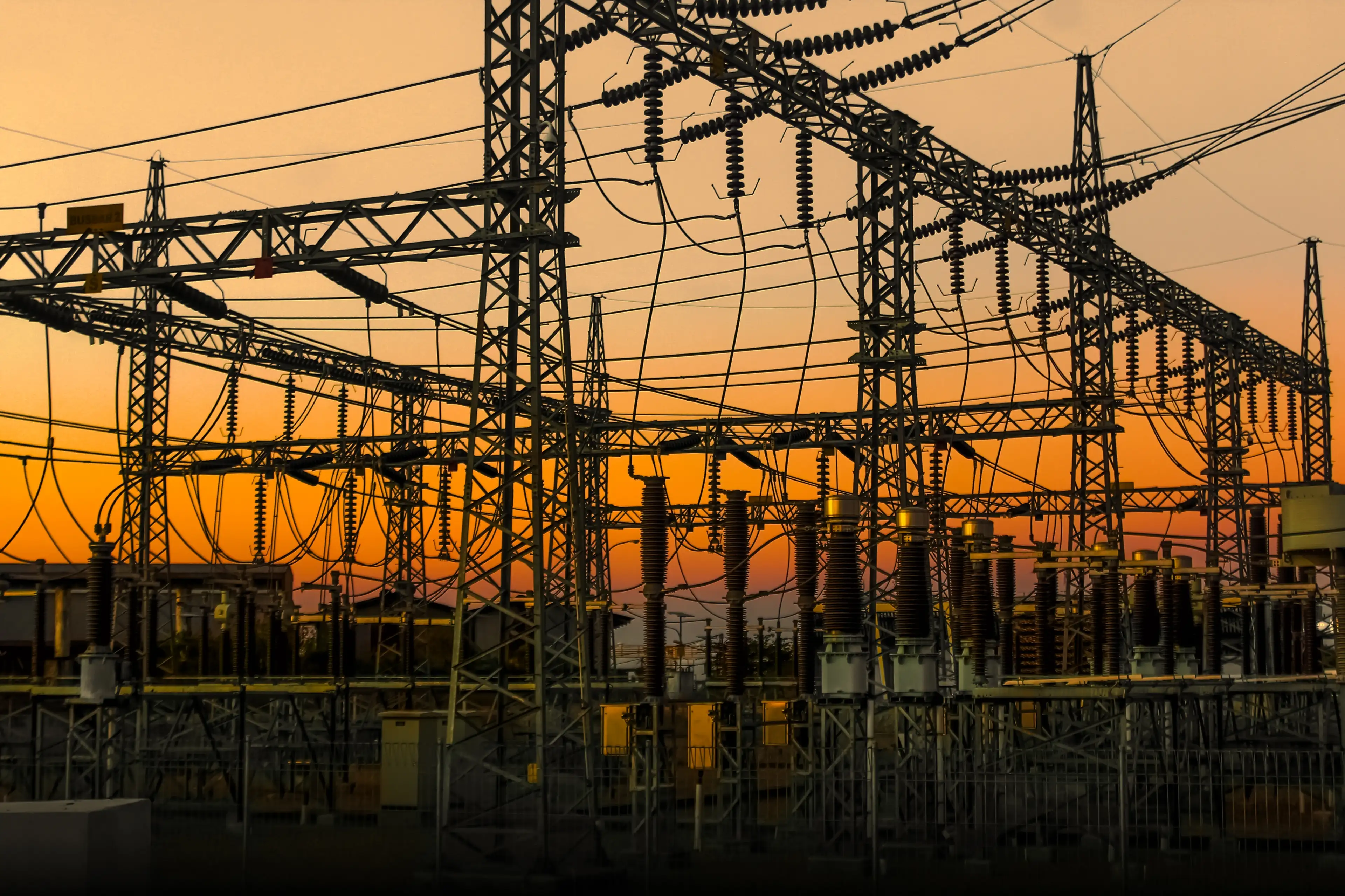 High-voltage transmission substation silhouetted against an orange sunset sky